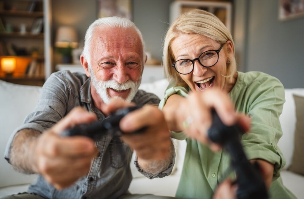 A close-up image of an older couple in personal care holding video game controllers and laughing.