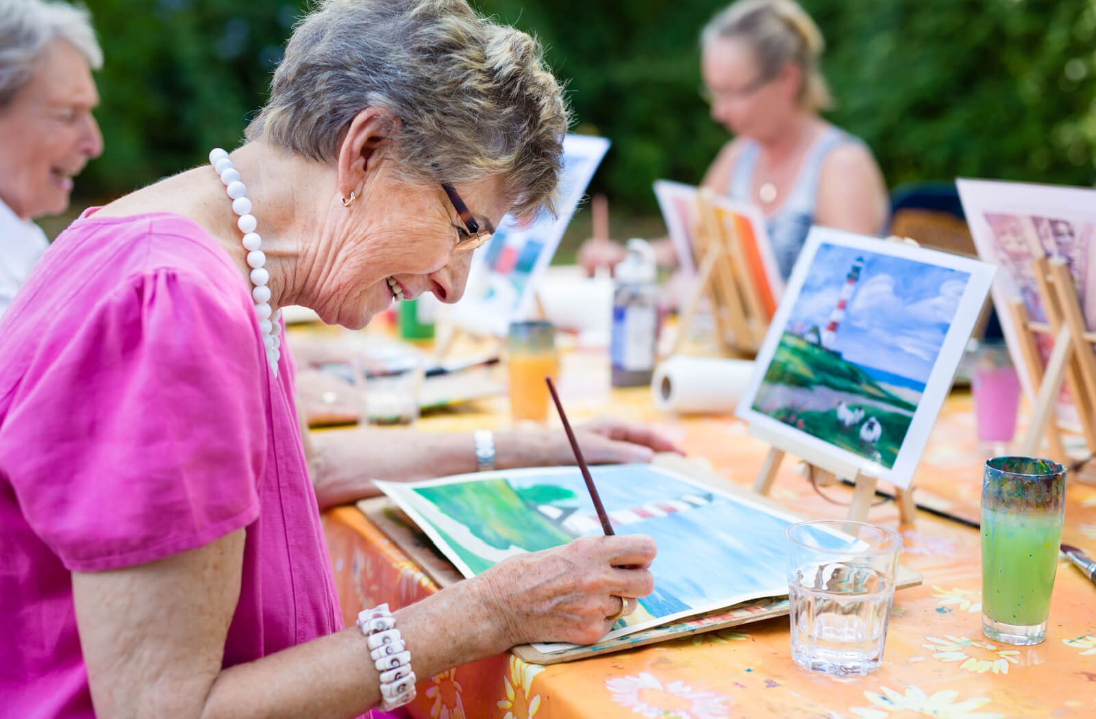 An older adult smiling while trying watercolor painting outdoors to see if it's the right hobby for them.