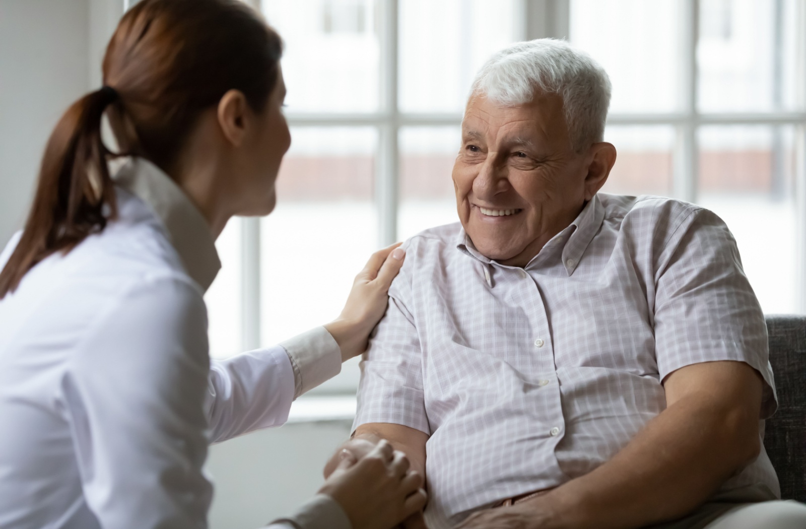 An older adult with dementia smiling as a caregiver reassures them during conversation.