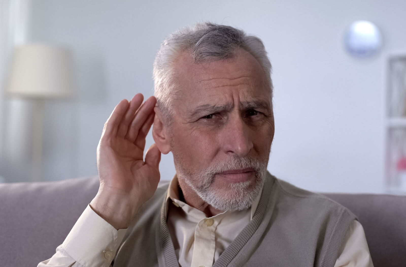 An older adult cups their hand behind their ear to hear better so they can respond verbally.