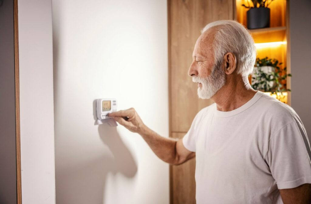 An older adult in their home adjusting the heating on a control on the wall.