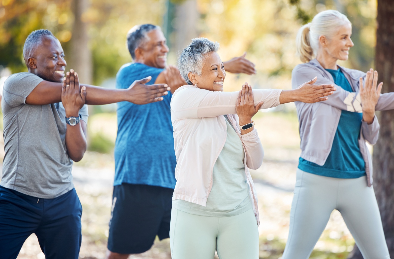 A group of 4 older friends doing tai chi in the park during summer and laughing.
