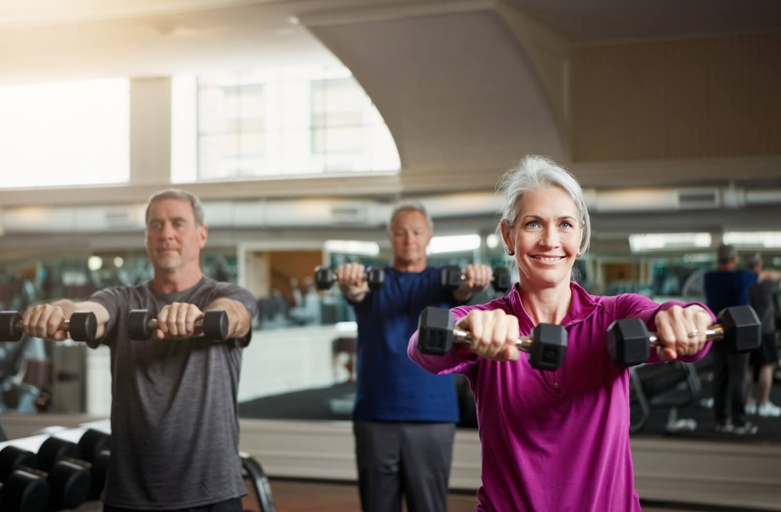 Three seniors lift light weights in a senior living exercise facility to help build muscle strength to reduce arthritis pain