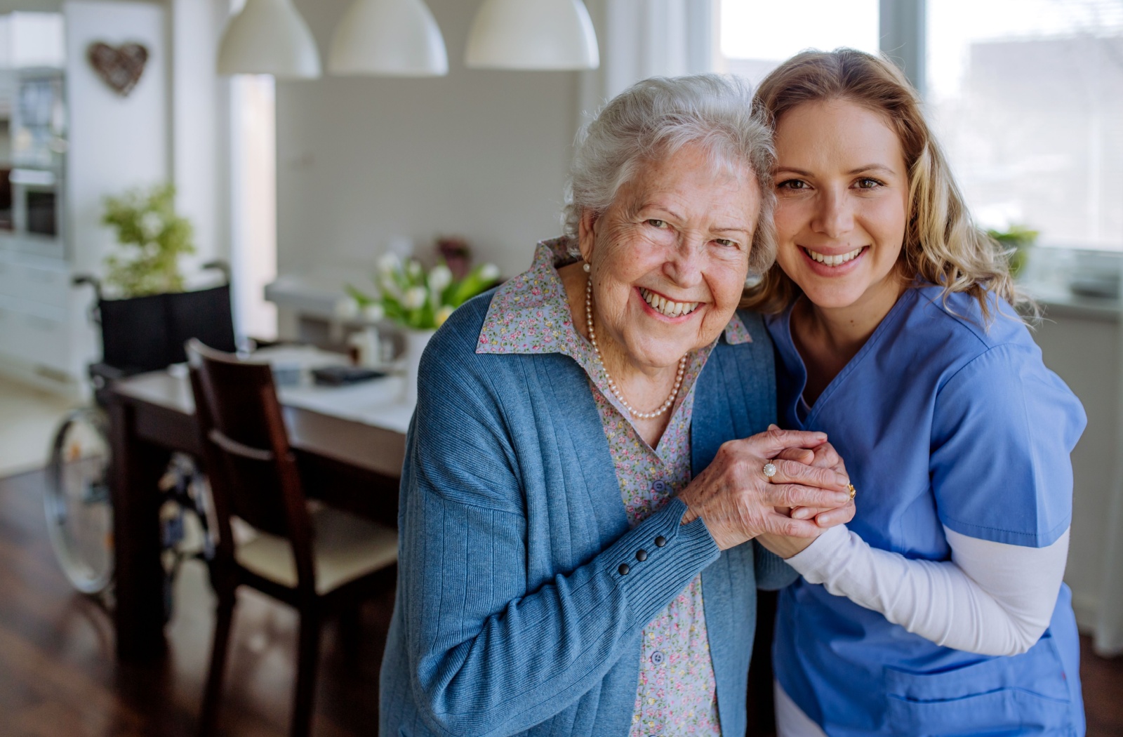 A smiling caregiver embraces and holds hands with a memory care resident